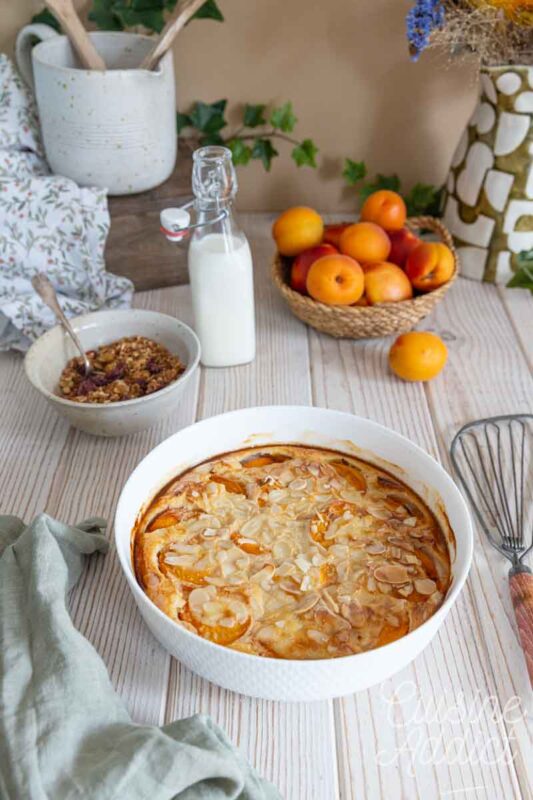 Petit déjeuner composé d'une part de clafoutis aux abricots, d'un verre de lait et de fruits frais.